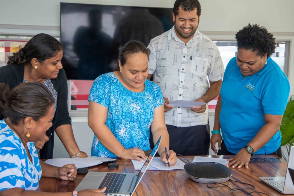 Georgina Naigulevu, Tetra Tech Associate Director of Disability Inclusion, Justice and Transformation, Info Pacific signs a document in a meeting with four team members from Fiji Program Support Facility.