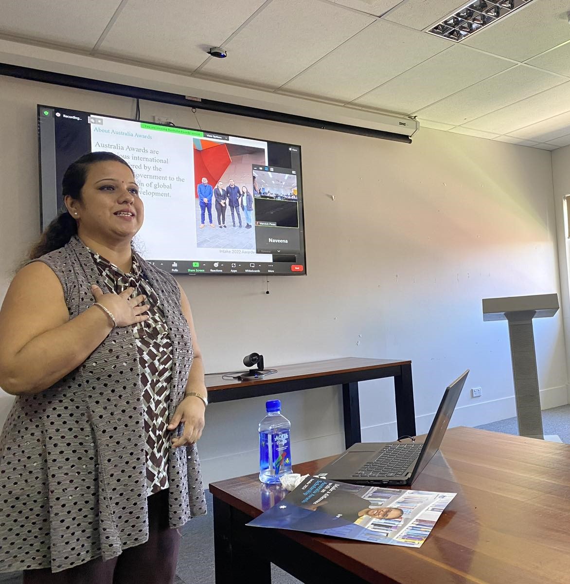 A woman stands in front of a screen, preparing to give a presentation.